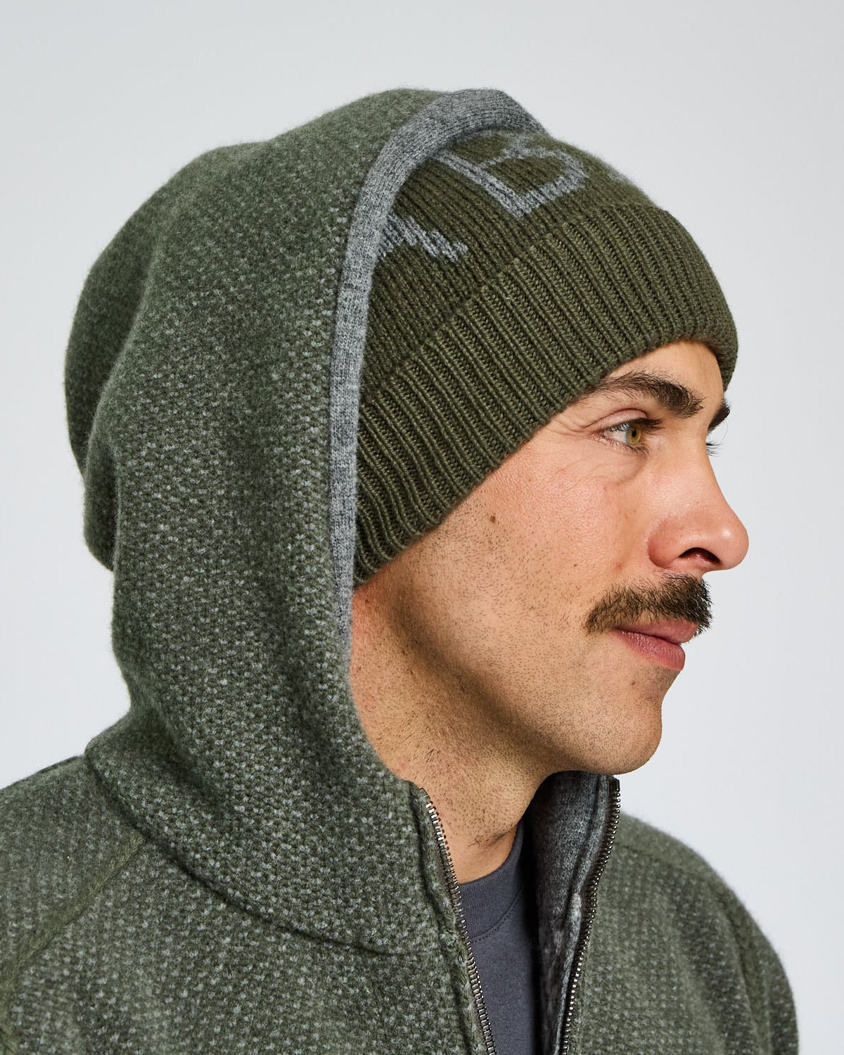Man wearing a green beanie and jacket on a plain background