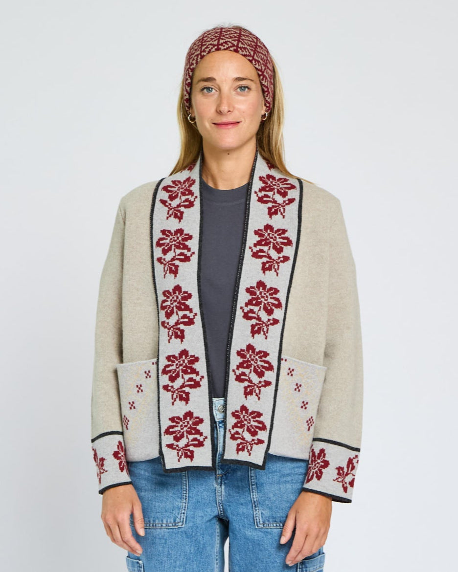 Woman wearing a patterned cardigan with floral designs on a plain background