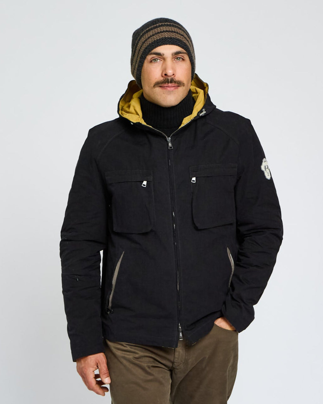 Man wearing a black jacket with yellow lining and a beanie on a white background