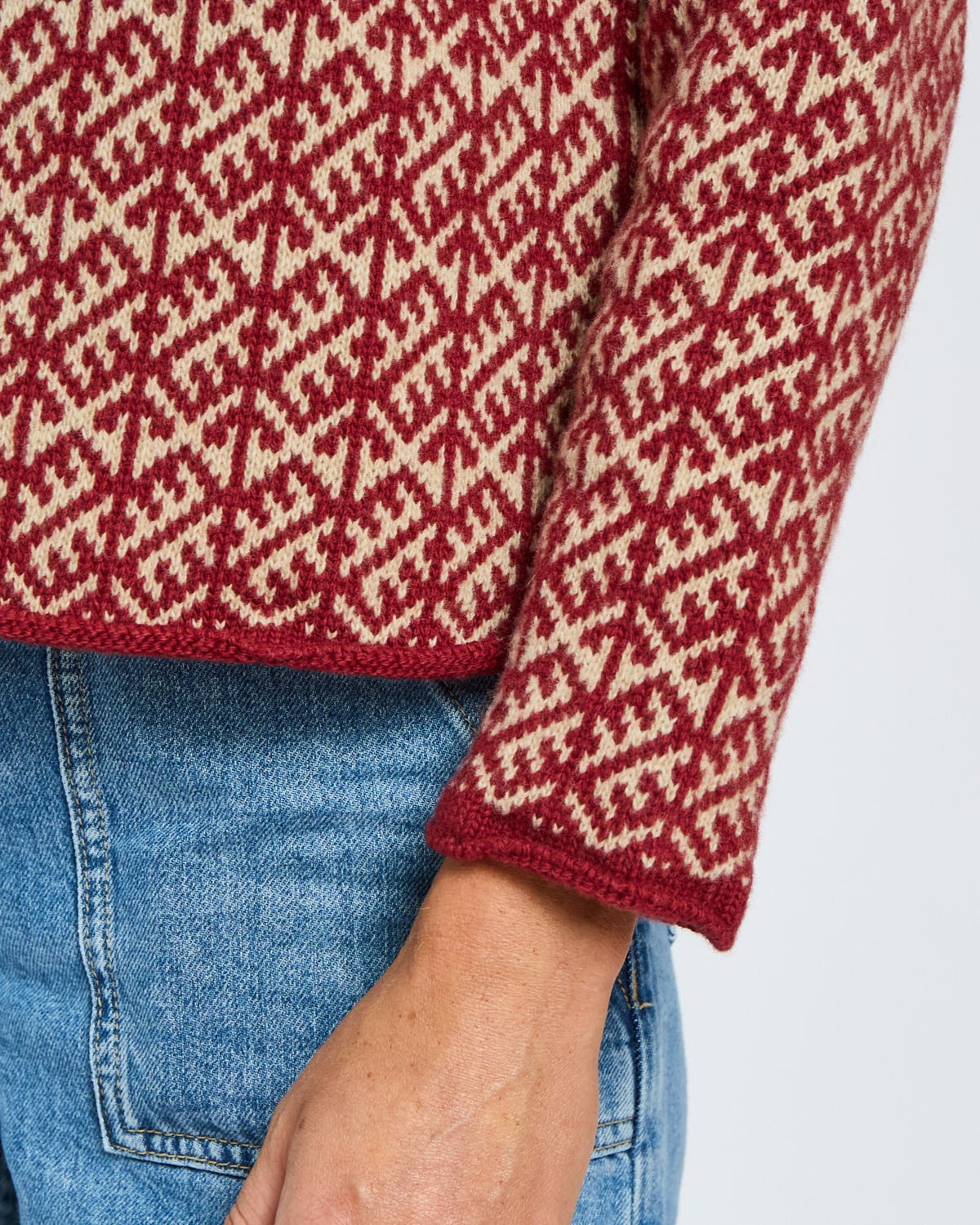 Red and white patterned sweater with blue jeans on a light gray background