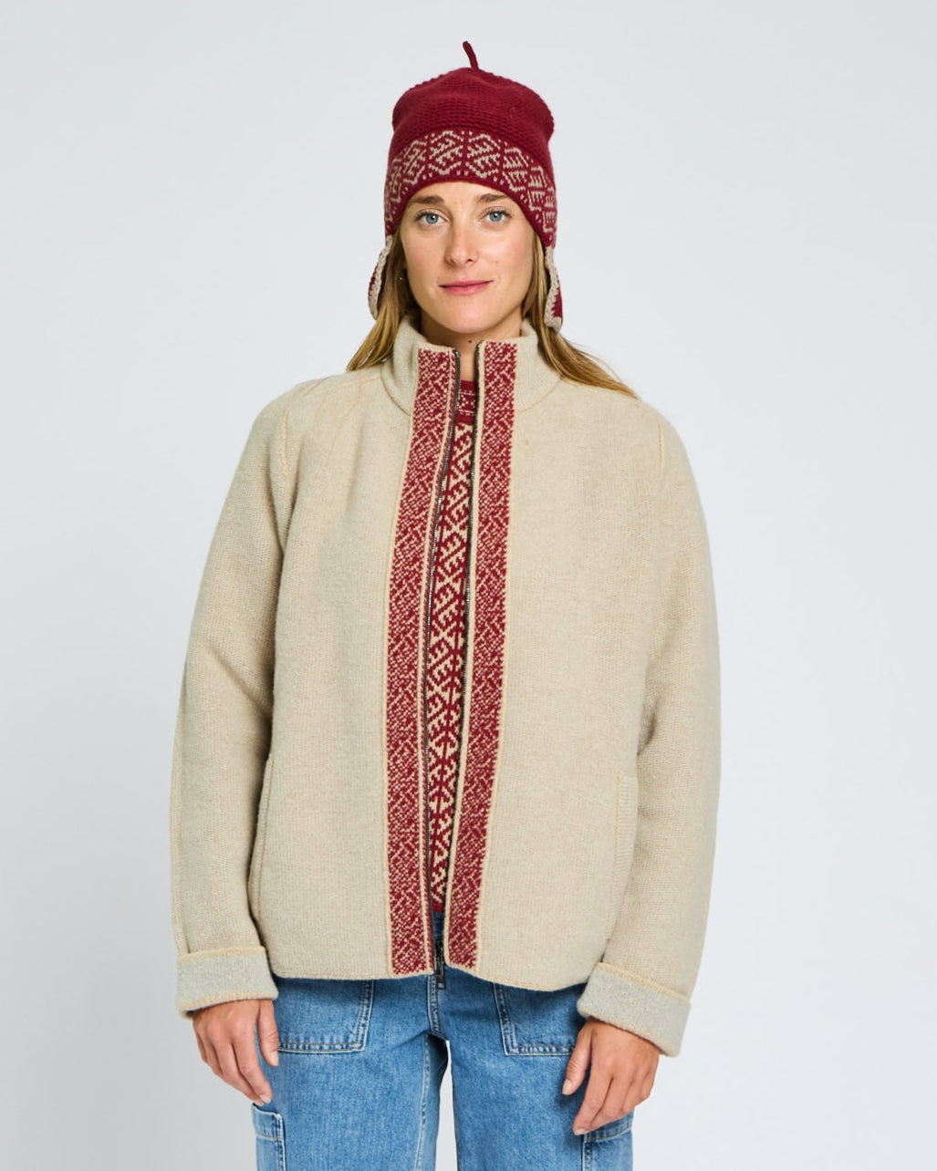 Person wearing a beige sweater with red patterns and a matching beanie on a white background