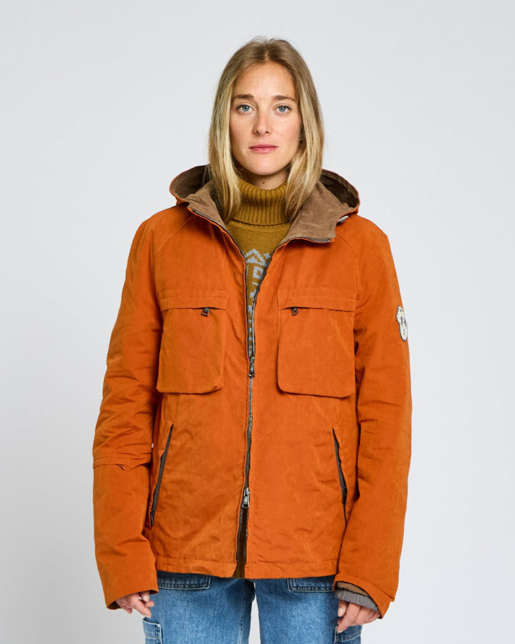 Person wearing an orange jacket with a hood on a plain background