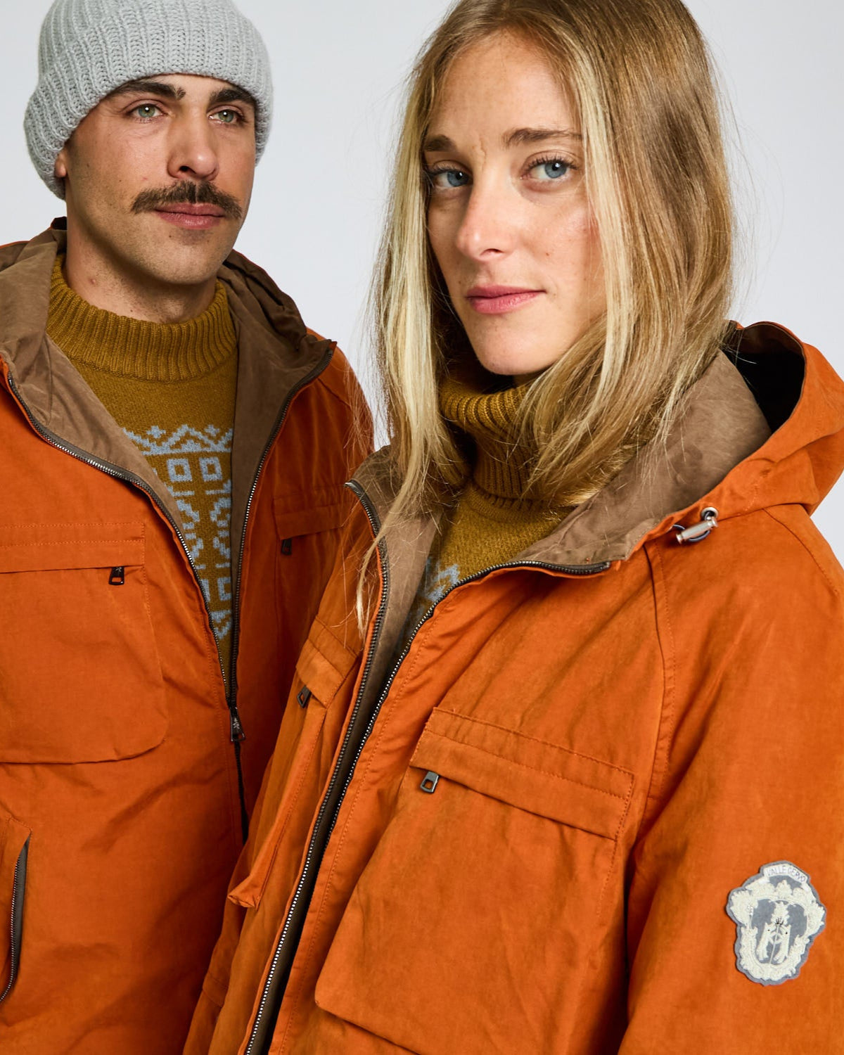 Two people wearing orange jackets with a plain background