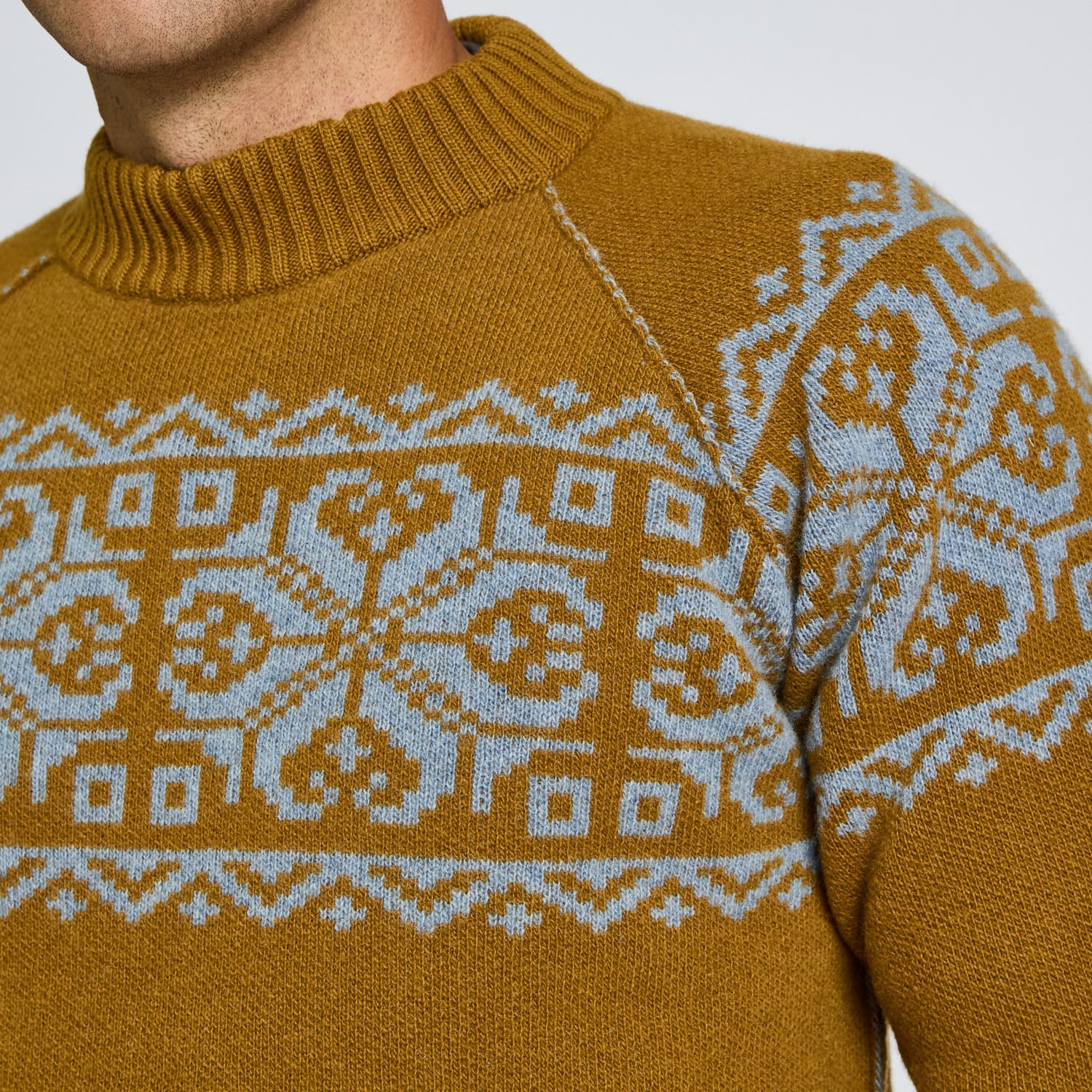 Close-up of a mustard yellow sweater with a white pattern on a neutral background