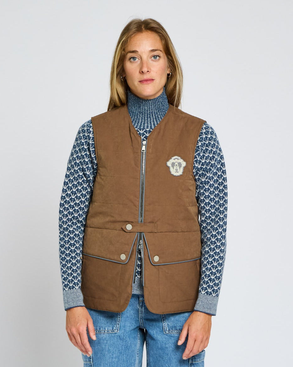 Person wearing a brown vest over a patterned shirt with a plain background
