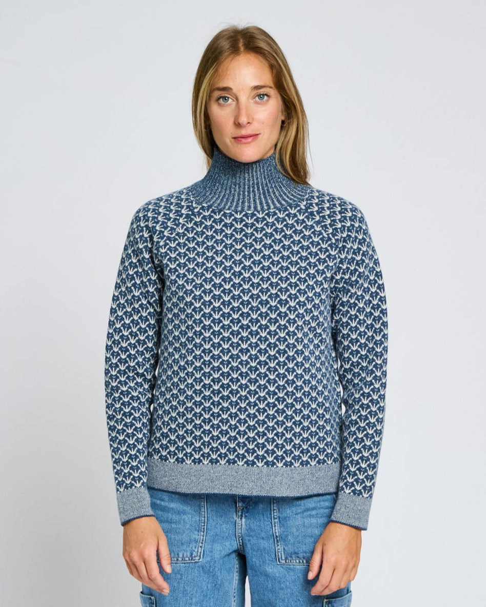 Person wearing a blue patterned sweater and jeans on a light gray background