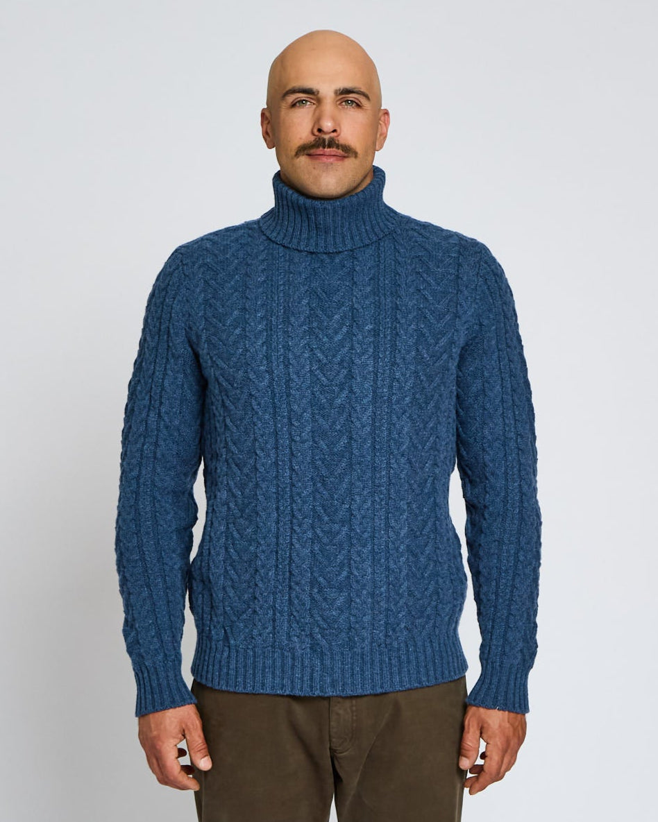 Man wearing a blue cable knit sweater against a white background