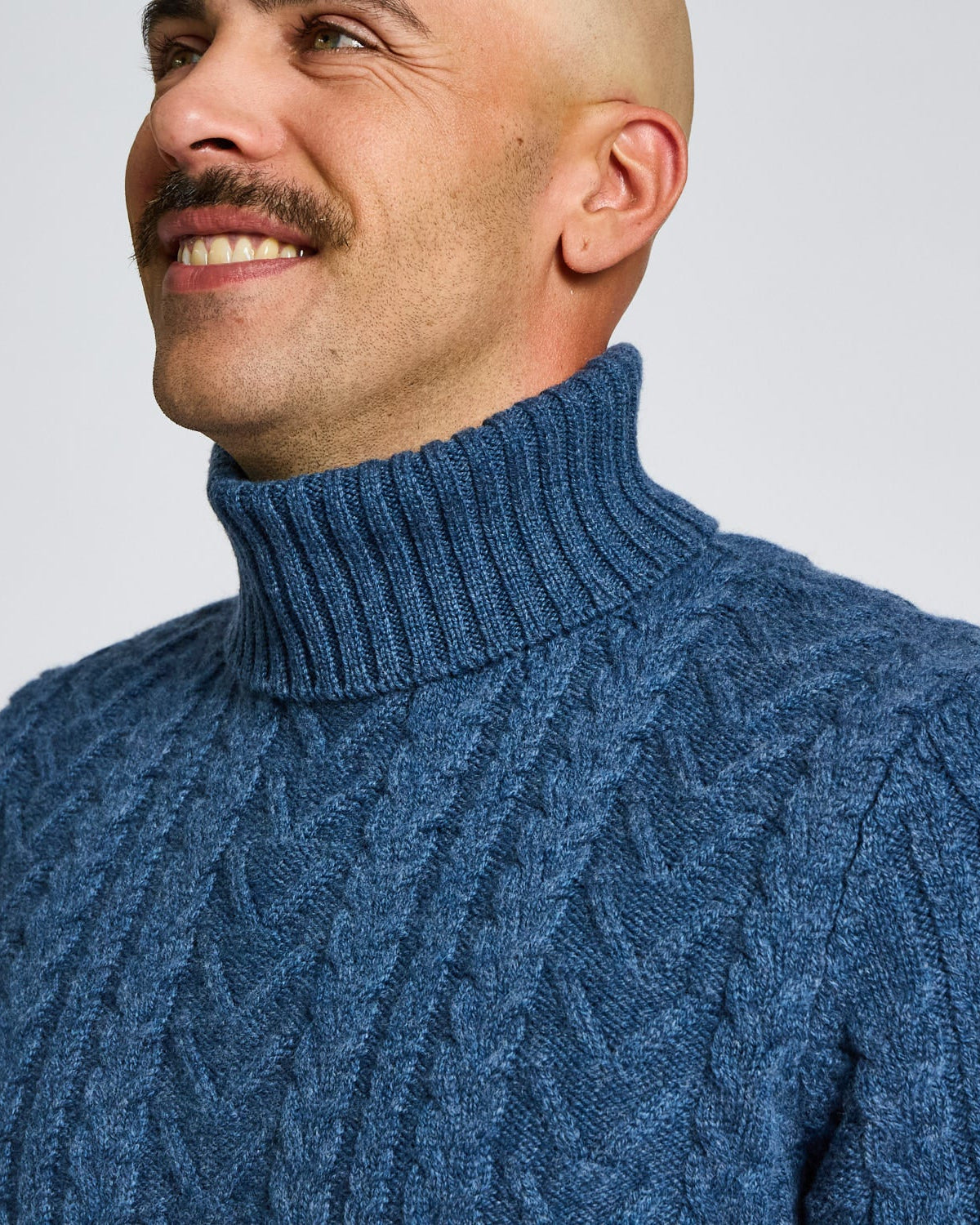 Man wearing a blue cable knit sweater against a plain background