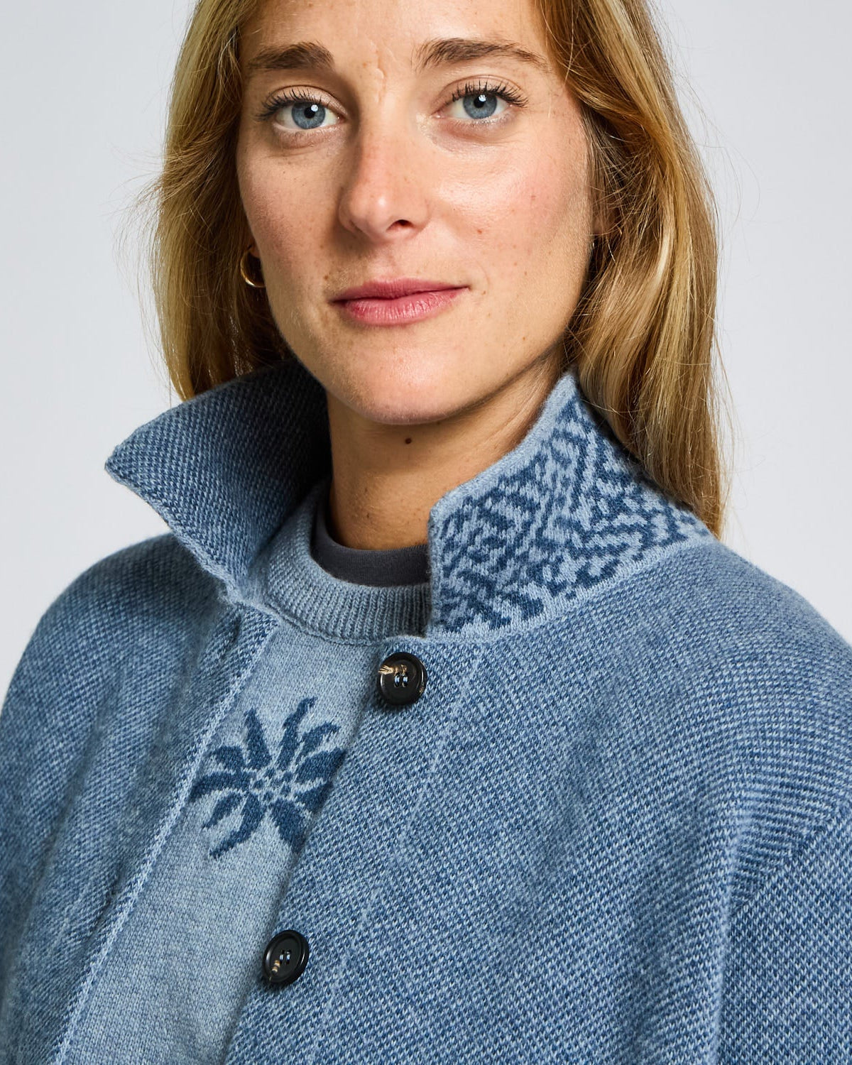 Person wearing a blue knitted sweater with a patterned collar against a plain background