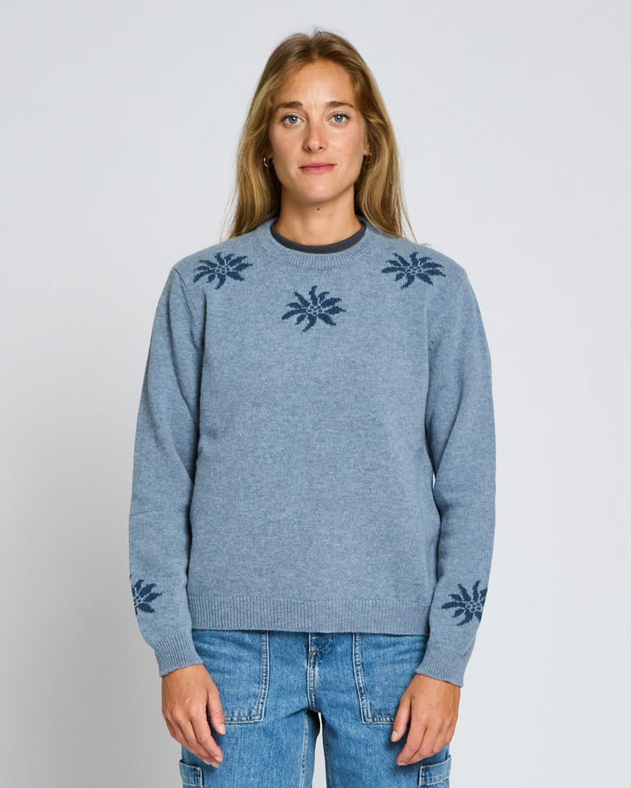 Person wearing a blue sweater with floral patterns on a plain background