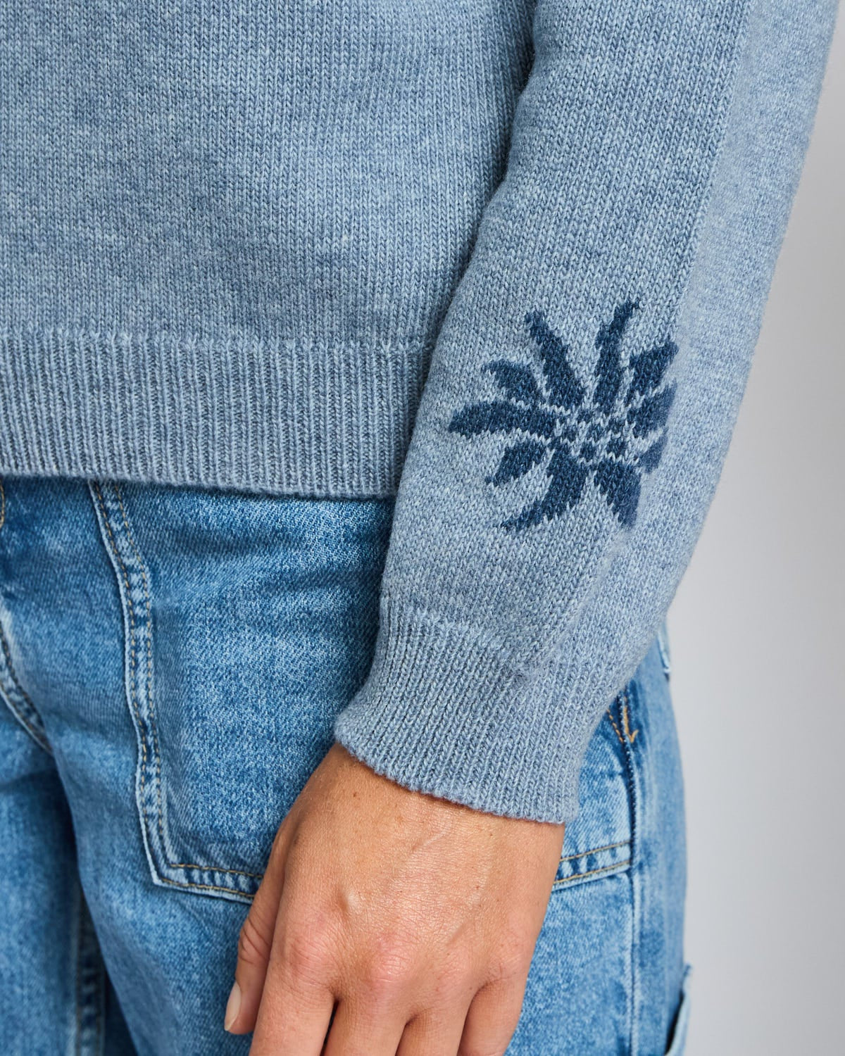 Close-up of a blue sweater with a floral pattern on the sleeve, worn with matching jeans.