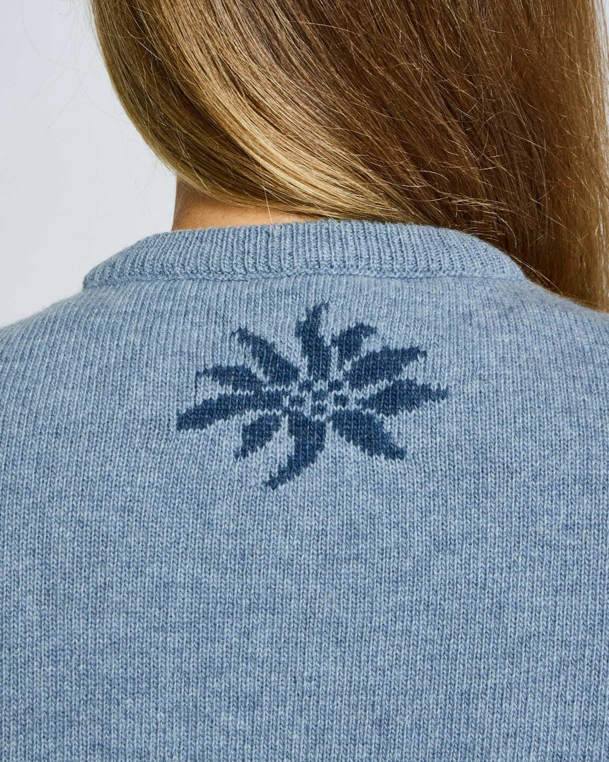 Blue sweater with a floral pattern on the back, worn by a person.