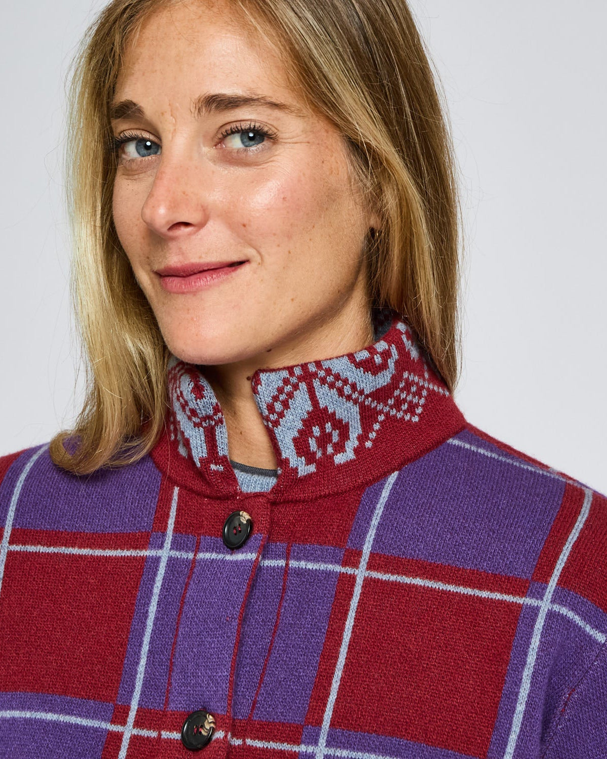 Person wearing a red and purple checkered jacket with a patterned collar against a plain background