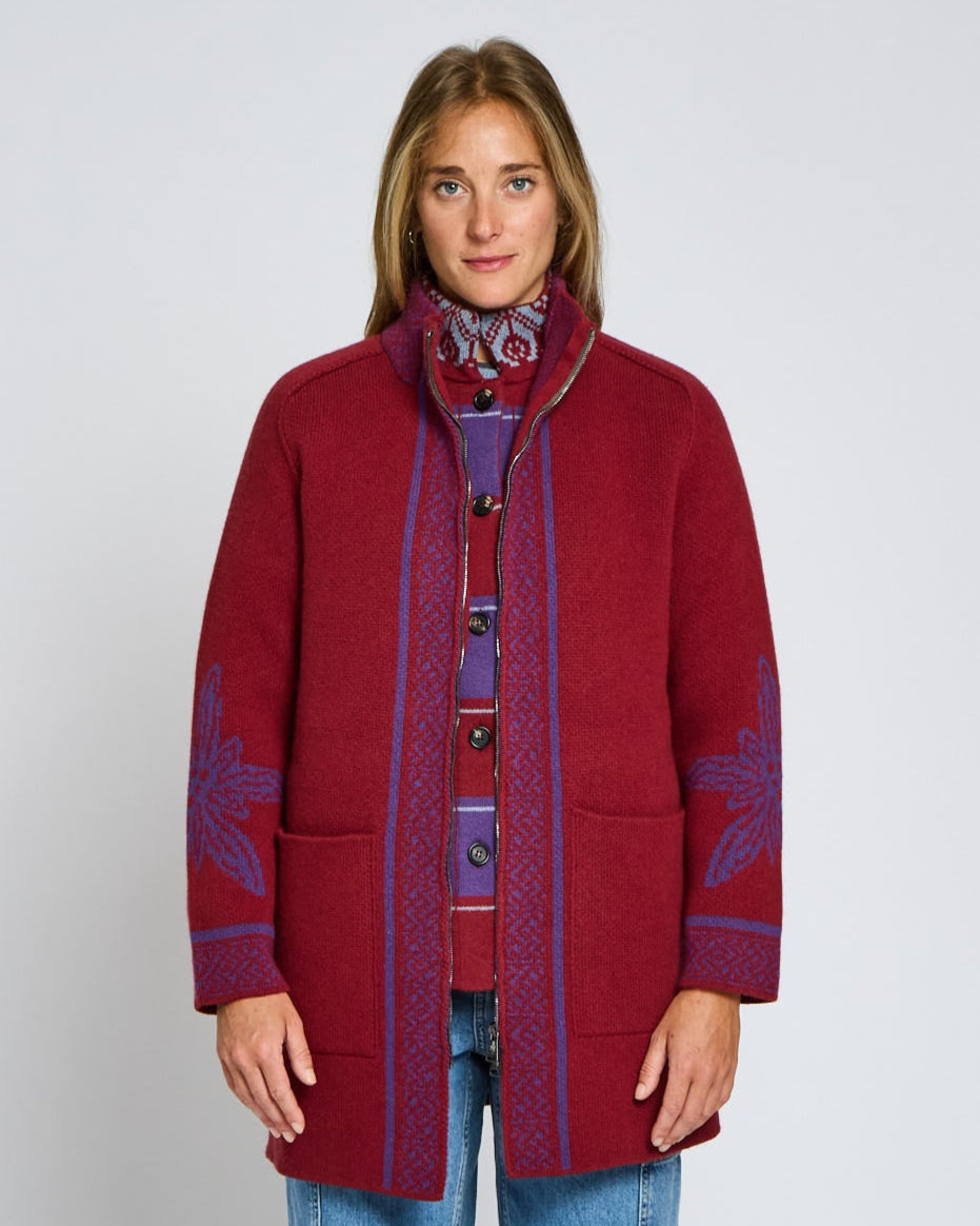 Person wearing a red coat with purple patterns on a plain background