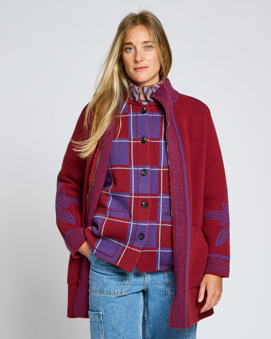 Woman wearing a red coat over a plaid shirt with a plain background