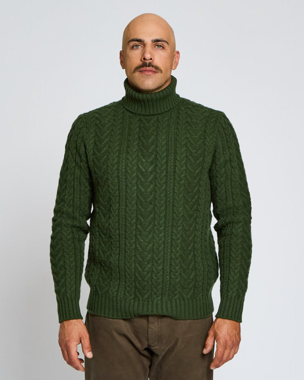 Man wearing a green cable knit sweater against a plain background