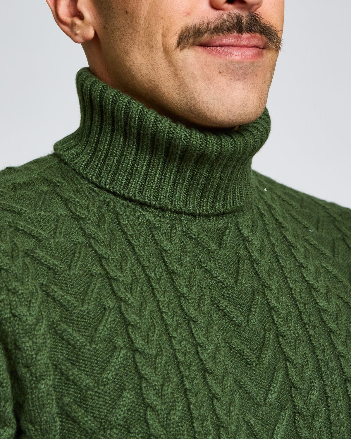Man wearing a green cable knit turtleneck sweater against a plain background