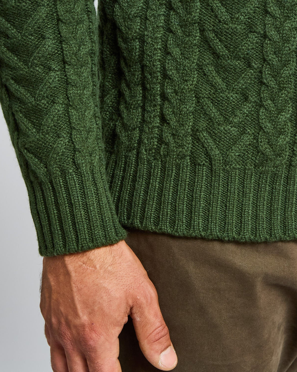 Close-up of a person wearing a green cable knit sweater with a neutral background
