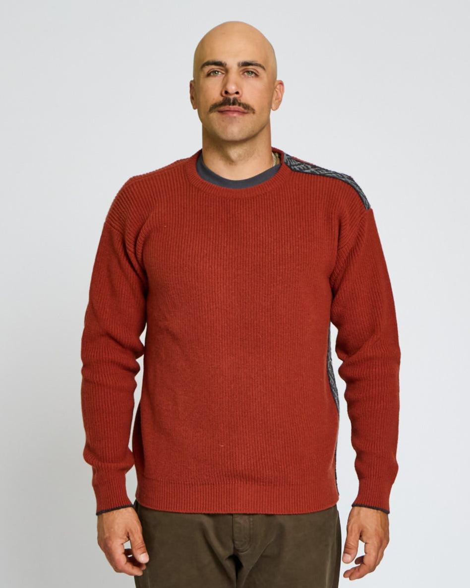 Man wearing a red sweater and brown pants against a plain background