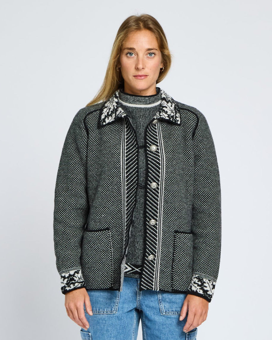 Person wearing a patterned jacket and jeans on a light gray background