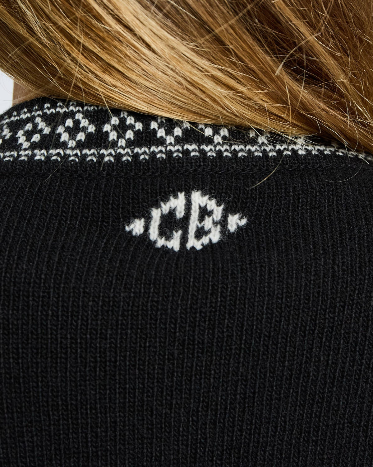 Black sweater with white patterned collar and 'CB' logo on a blurred background