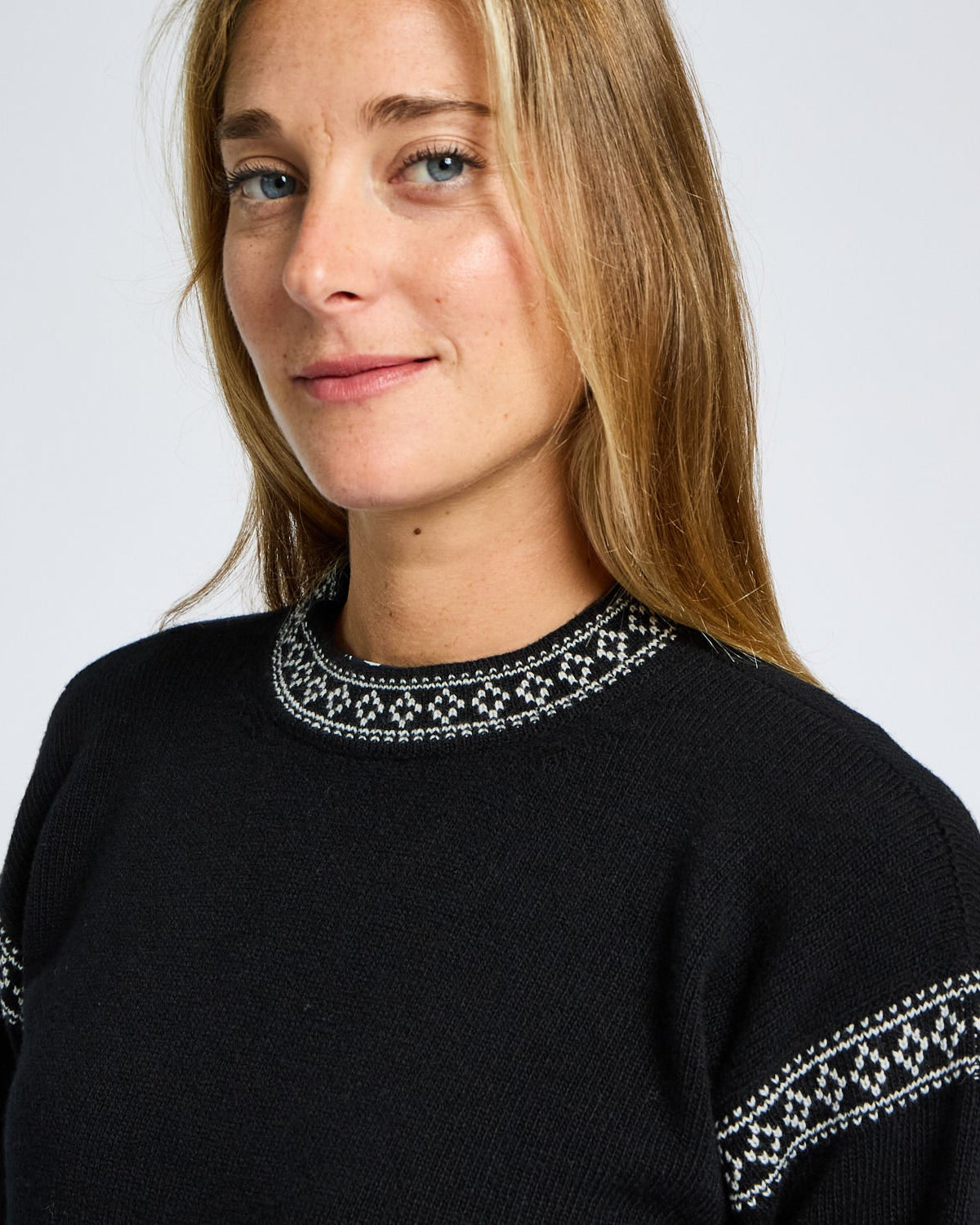 Woman wearing a black sweater with white embroidery on a plain background