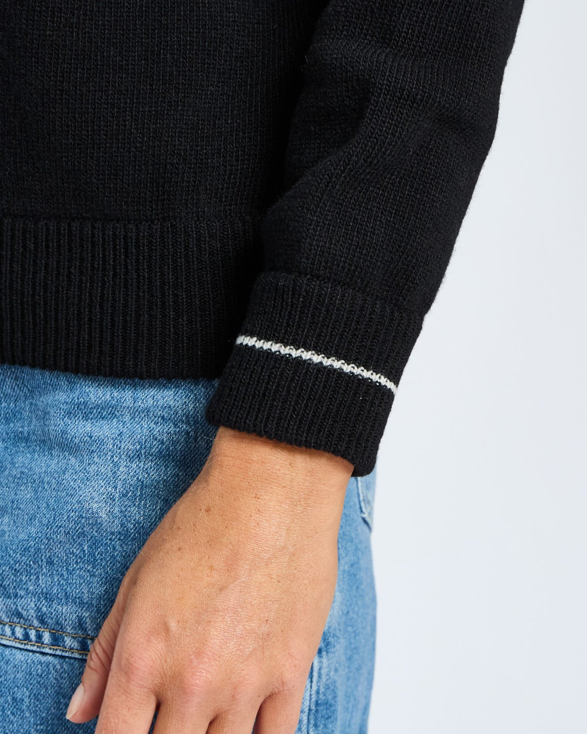 Black sweater with white trim on sleeve worn by a person, against a light gray background
