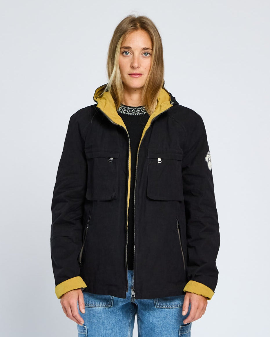 Person wearing a black jacket with yellow accents on a light gray background