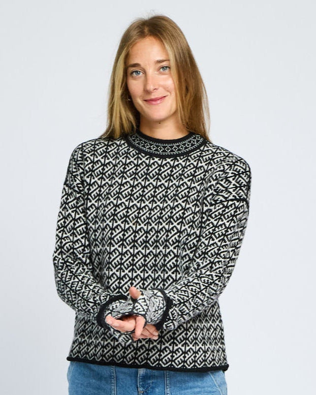 Person wearing a patterned sweater and blue jeans on a white background