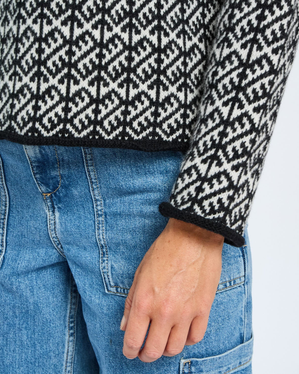 Person wearing a black and white patterned sweater and blue jeans on a light gray background