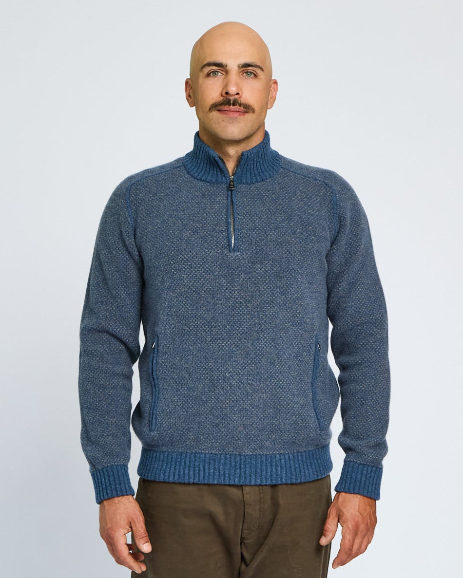 Man wearing a blue sweater with a quarter zip on a light gray background