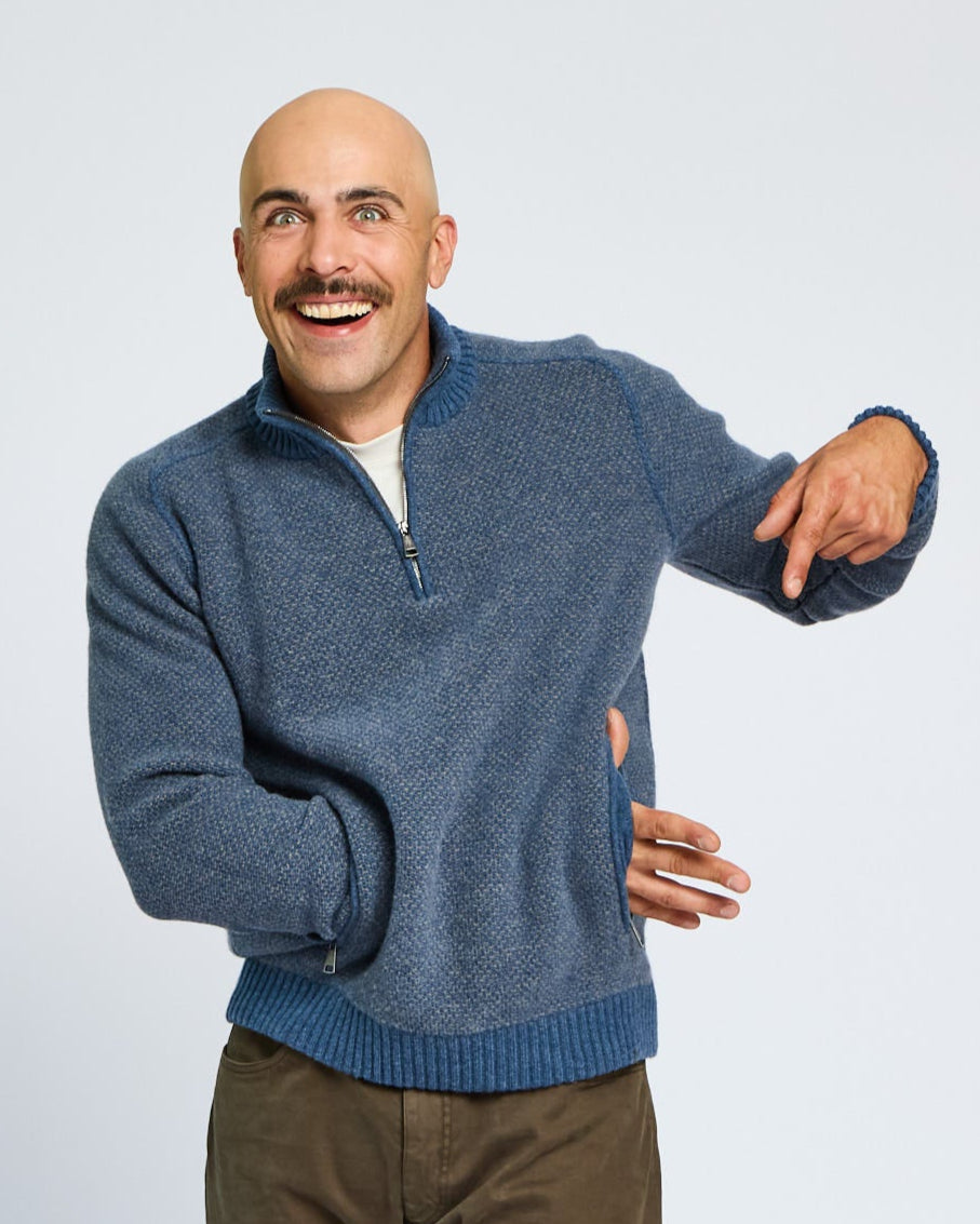 Man wearing a blue sweater pointing to his arm on a light gray background