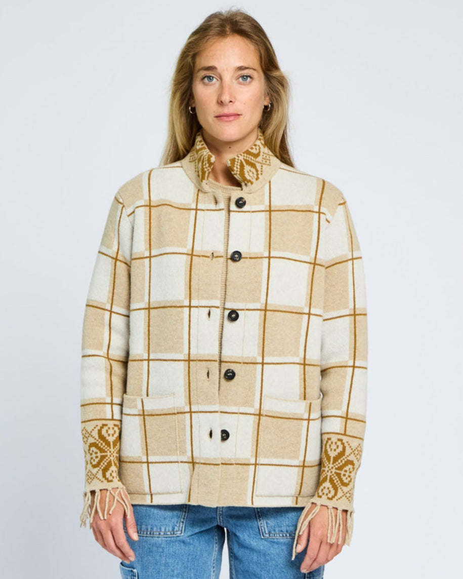 Woman wearing a beige and white checkered jacket with decorative cuffs on a plain background