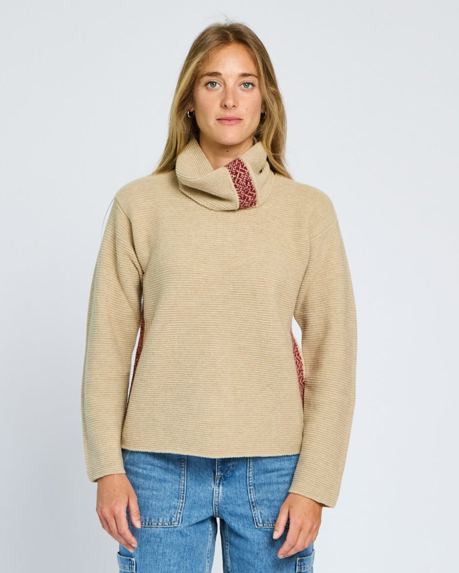 Woman wearing a beige sweater with a cowl neck and blue jeans on a white background