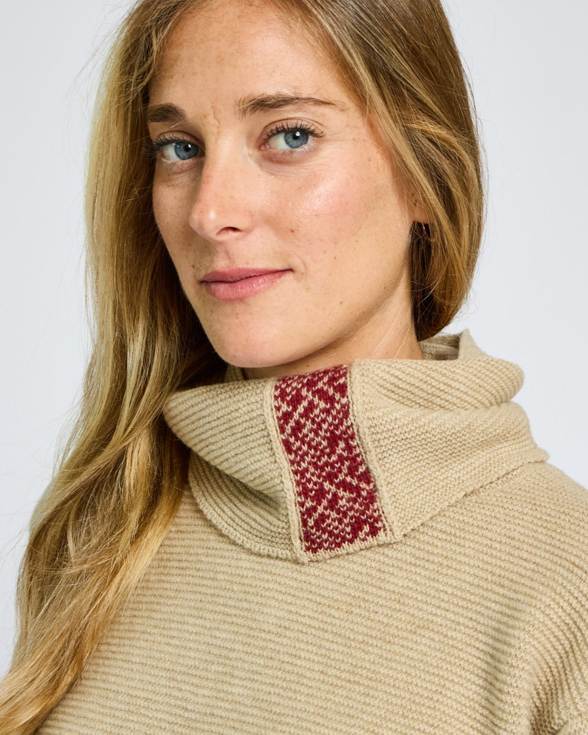 Woman wearing a beige sweater with a red patterned collar against a white background