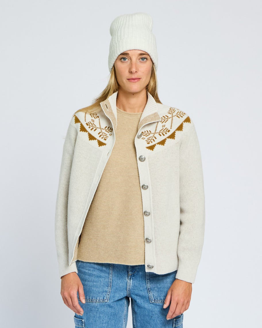 Woman wearing a cream cardigan with embroidery, beige sweater, and blue jeans on a light gray background