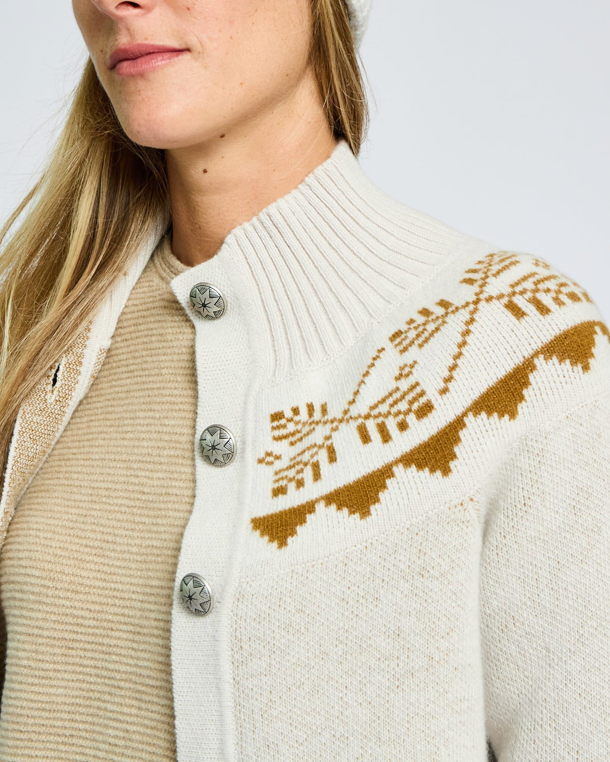 Close-up of a person wearing a cream-colored cardigan with brown pattern and silver buttons.