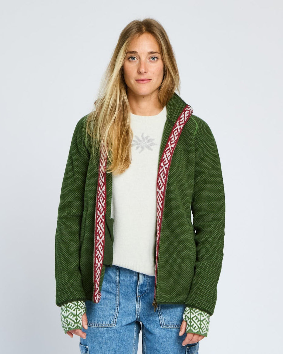 Woman wearing a green jacket with red and white patterned trim on a plain background