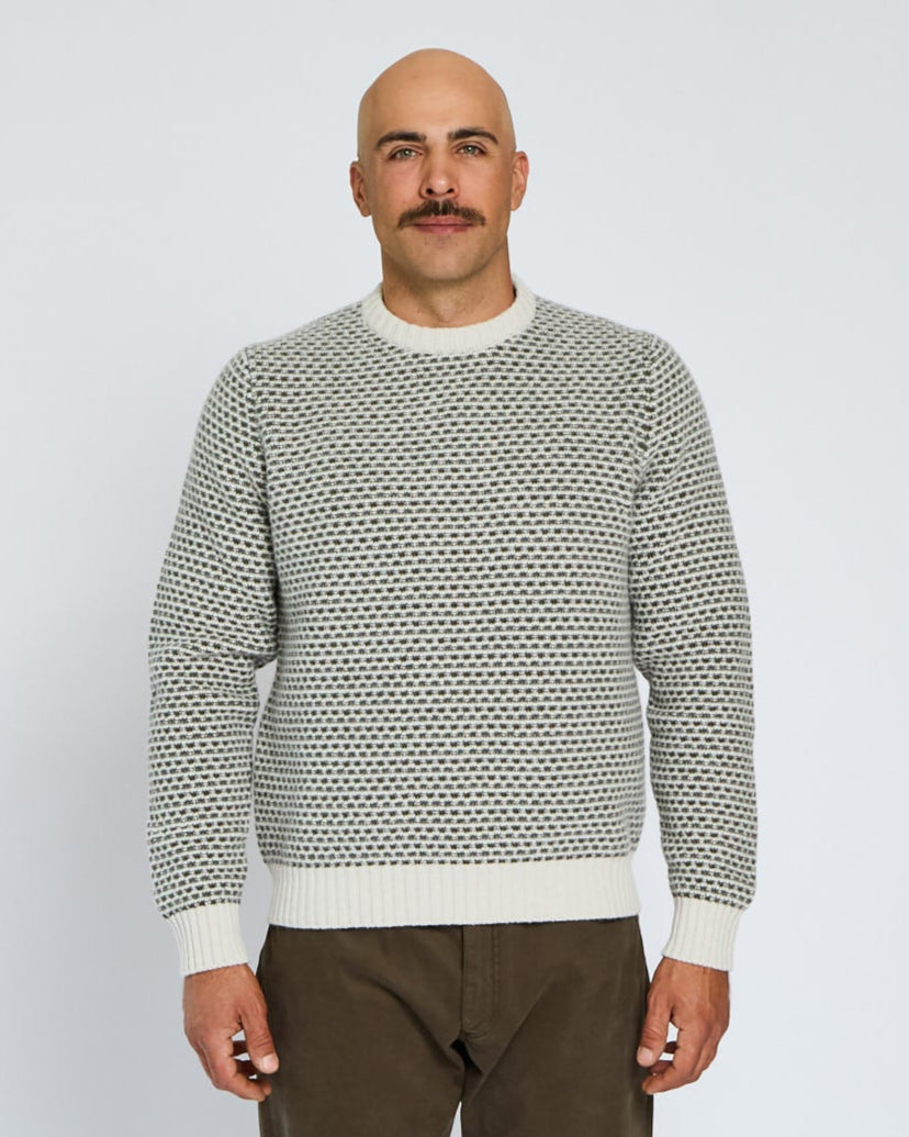 Man wearing a patterned sweater and brown pants against a white background