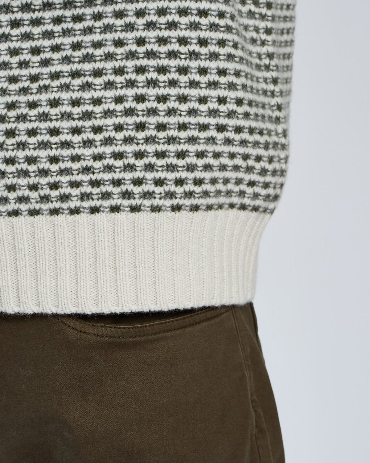 Close-up of a person wearing a black and white patterned sweater with brown pants on a light gray background