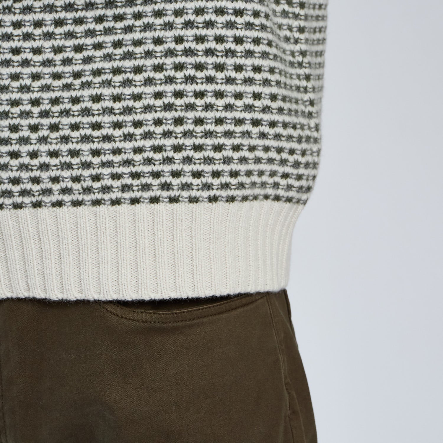 Close-up of a person wearing a black and white patterned sweater with brown pants on a light gray background