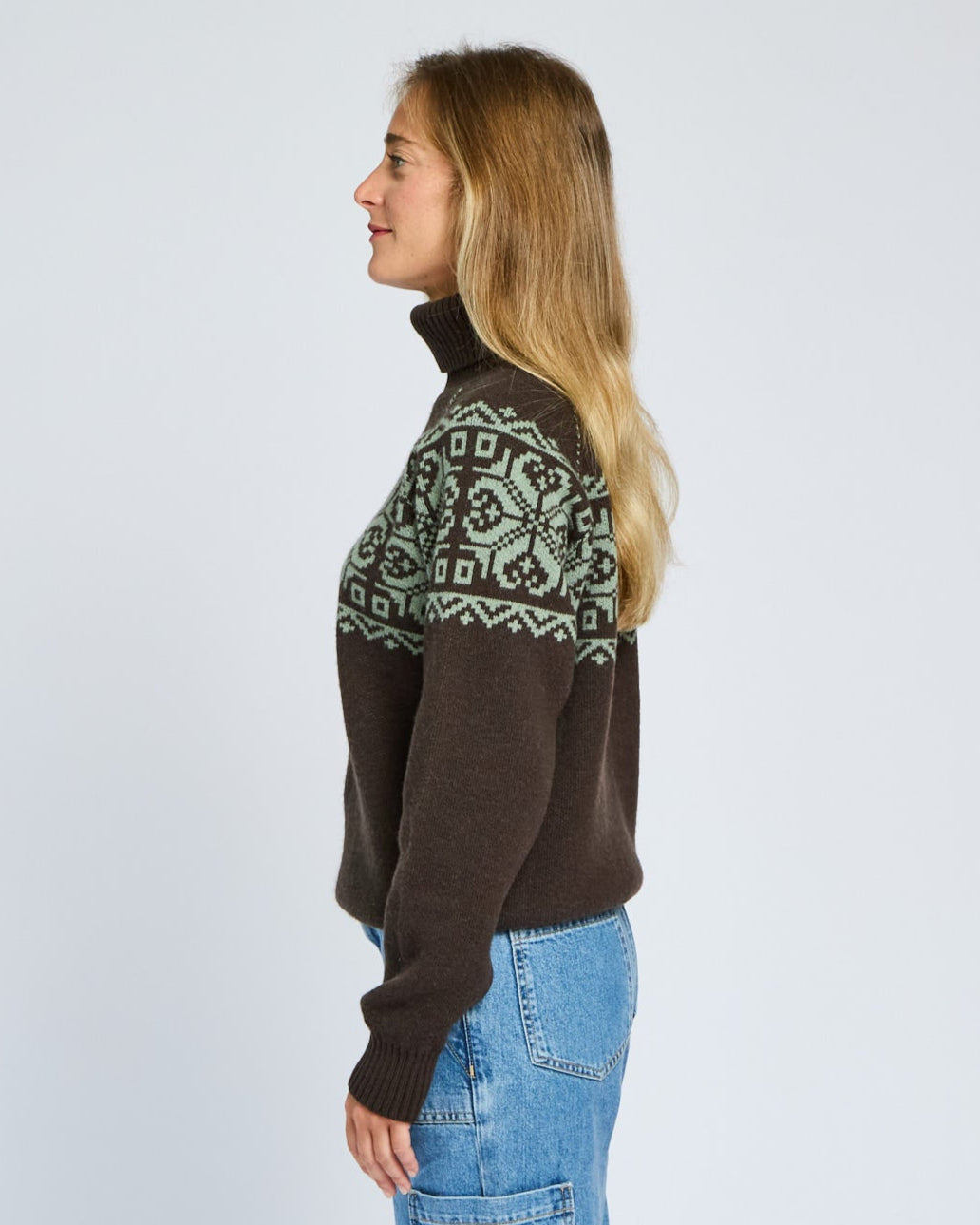 Woman wearing a brown sweater with green pattern on a light gray background