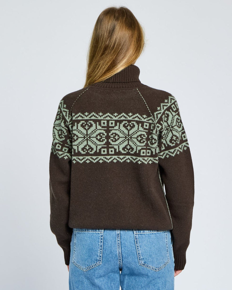 Person wearing a brown sweater with green patterns on a plain background
