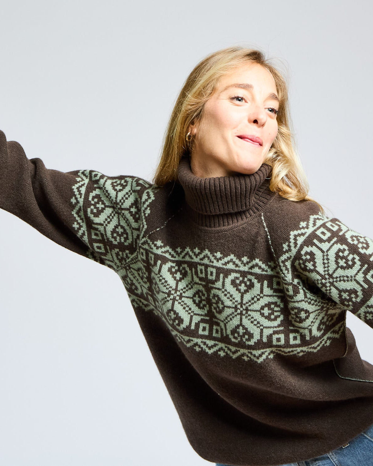Woman wearing a brown sweater with green patterns on a plain background