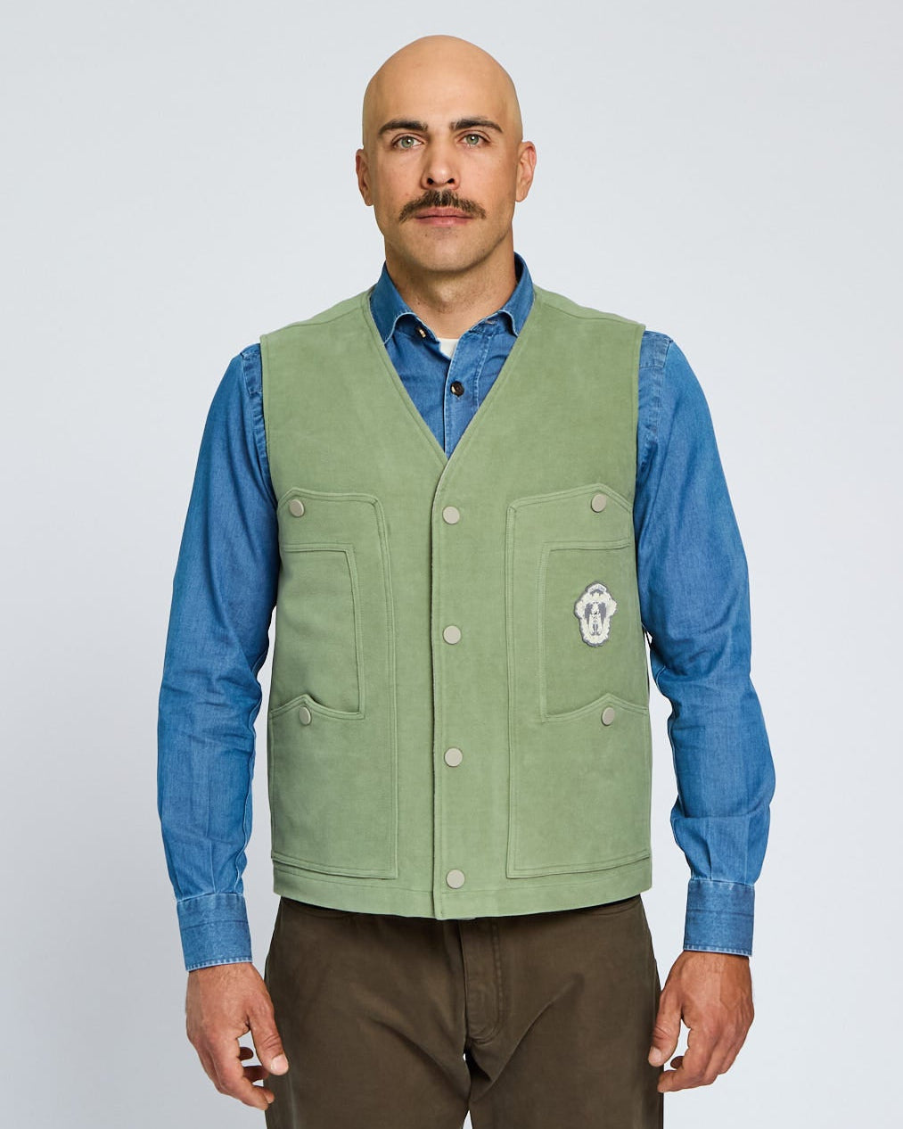 Man wearing a green vest over a blue shirt on a white background