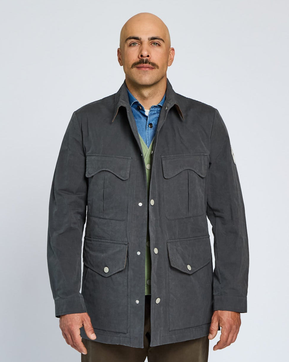 Man wearing a dark gray jacket over a blue shirt on a light gray background