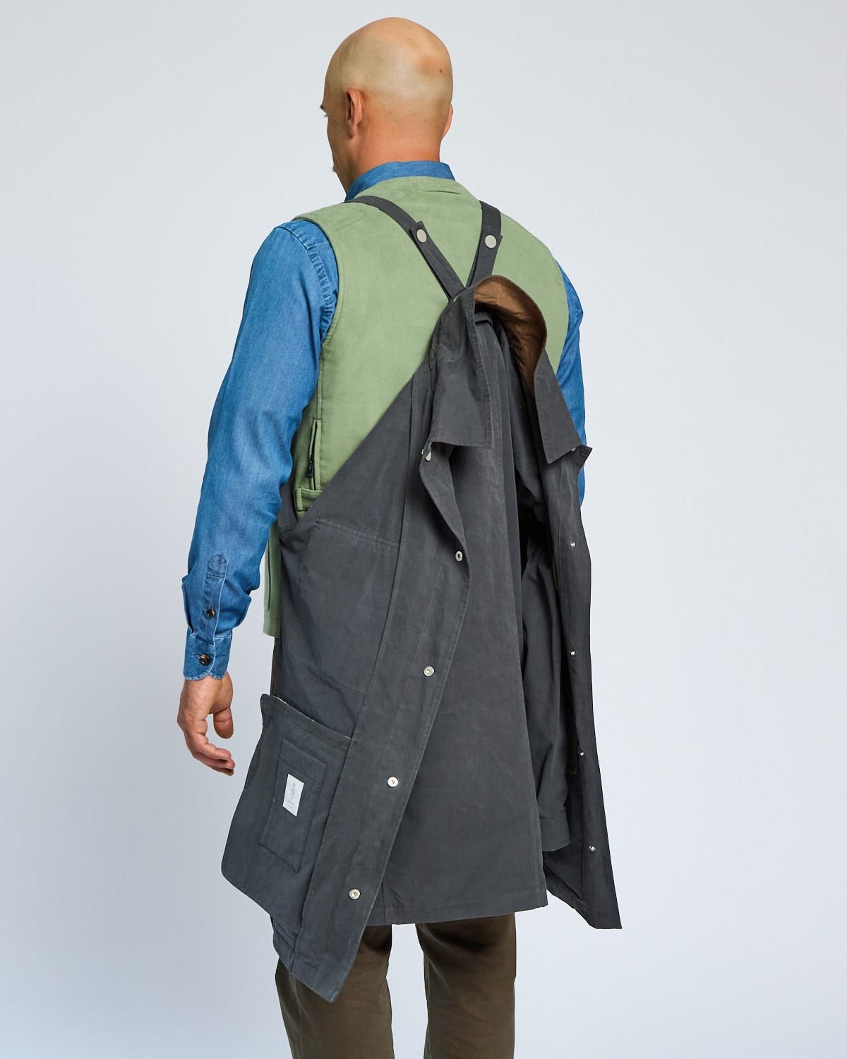 Person wearing a long gray coat over a blue shirt with a green vest on a light gray background