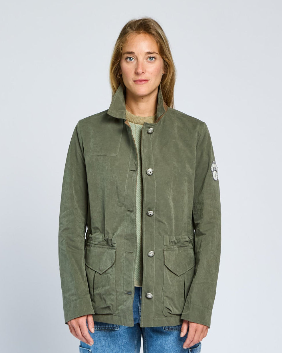 Person wearing a green jacket with a brand logo on a light gray background