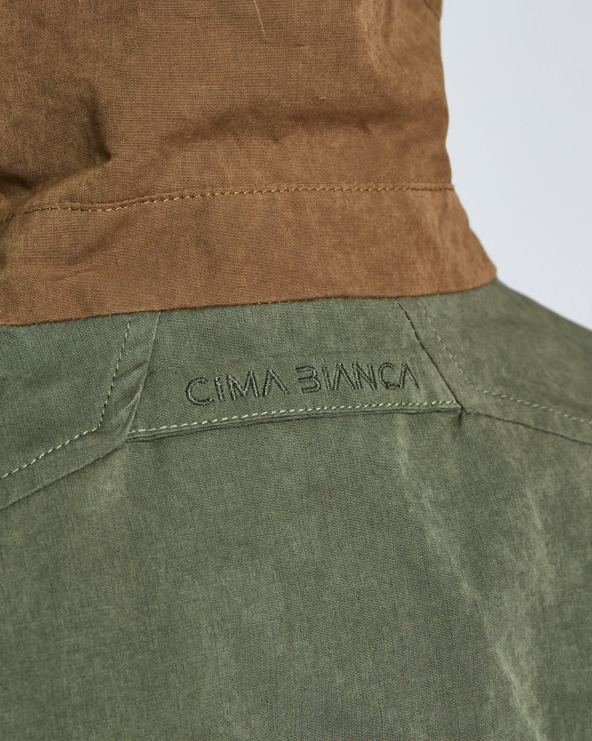 Close-up of a green jacket with a brown hood and 'Cima Bianca' branding.