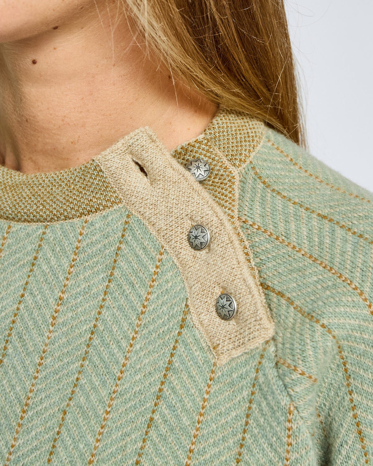 Close-up of a green textured garment with a beige collar and buttons on a white background